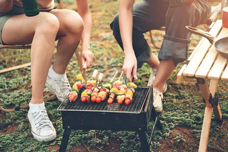 Horizontal image of a couple cooking kebabs on a barbecue outdoors.