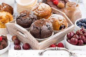 Horizontal image of a tray full of baked goods next to fresh fruit.
