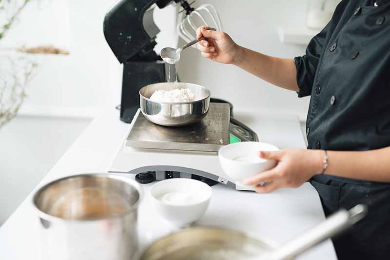 Horizontal image of a pastry chef measuring ingredients on a scale.