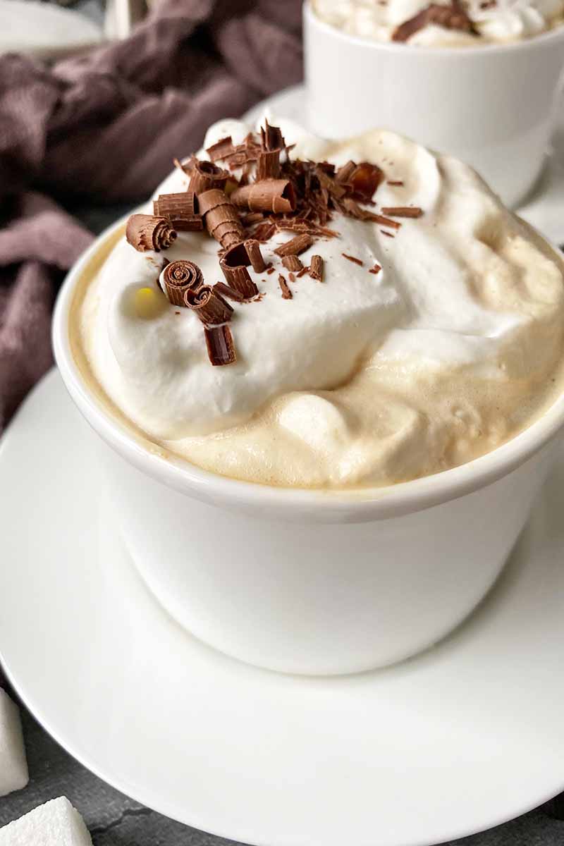 Vertical close-up image of a white cup on a plate filled with assorted garnishes.