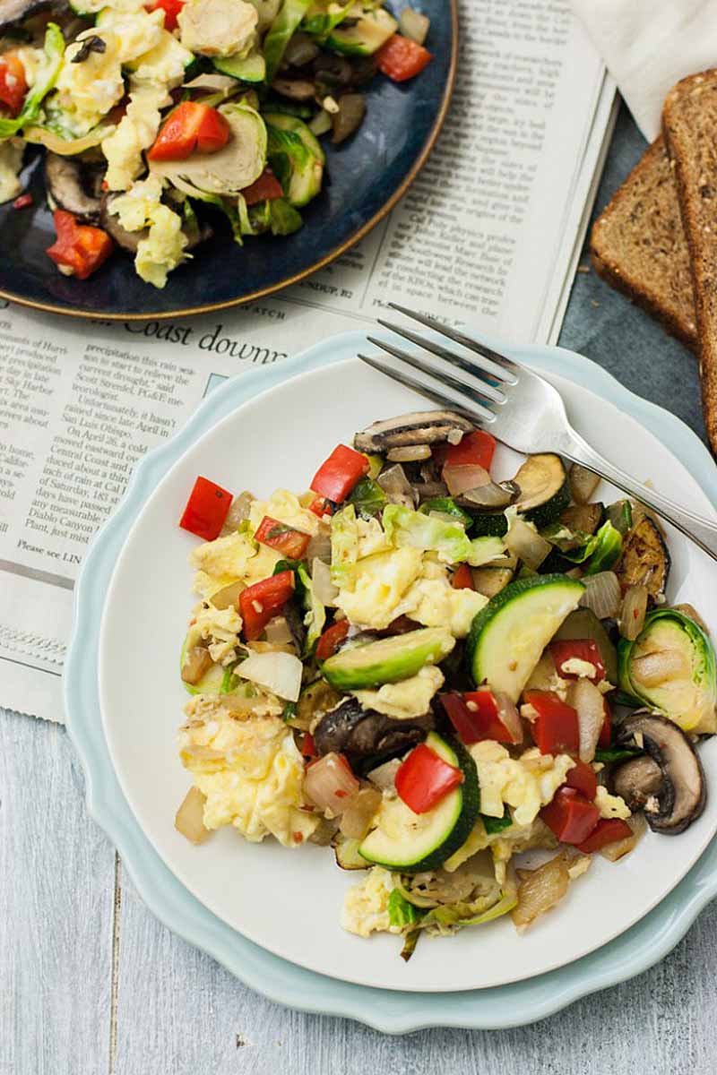 Top down view of a white ceramic plate full of a Super Veggie Breakfast Scramble made with sliced veggies and scrambled eggs.