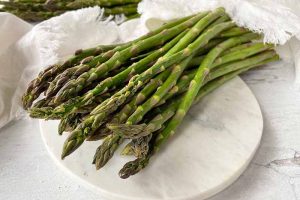 Horizontal image of a pile of fresh green vegetables on a white marble surface next to white towels.
