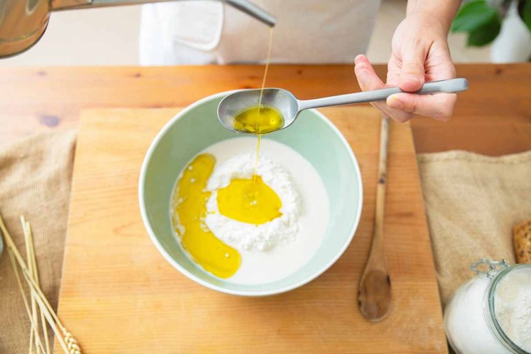 Horizontal image of measuring liquid ingredients into a bowl with flour on a wooden cutting board.