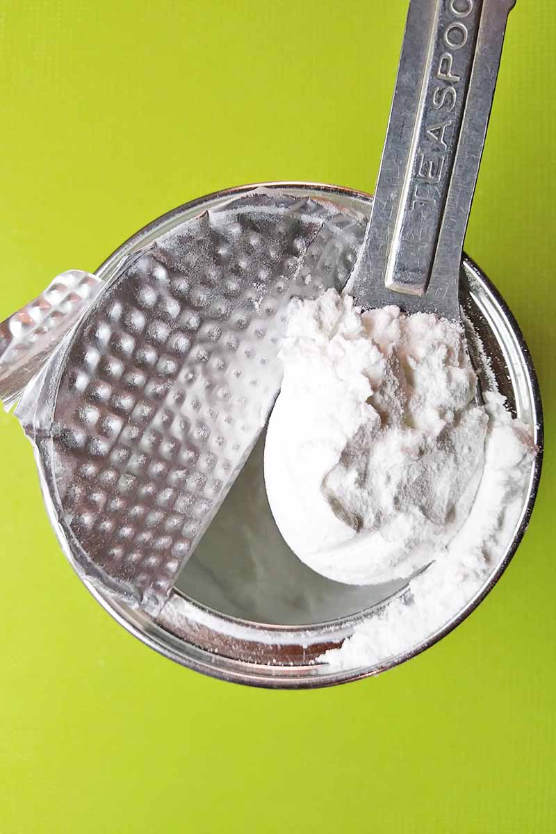 Vertical image of measuring out a dry leavening agent in a can on a green background.
