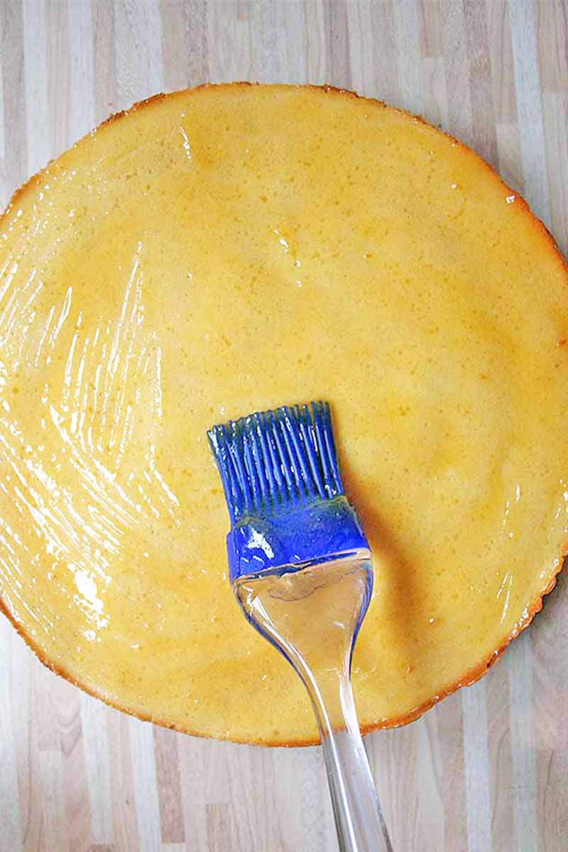 Vertical image of applying glaze on a cake round.