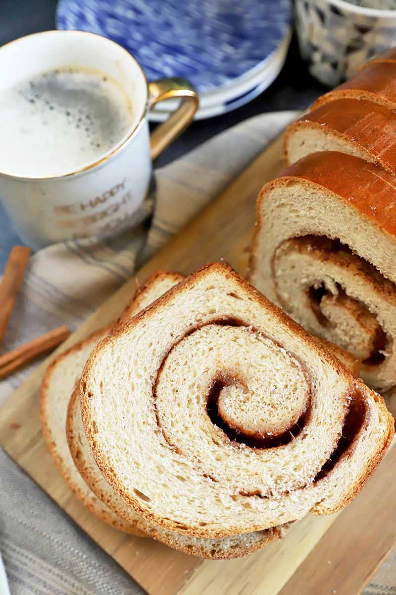 Vertical image of fluffy bread slices with a swirl filling stacked on top of each other next to plates and mugs of coffee.