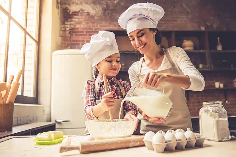 Horizontal image of a mother and daughter in chef's hats mixing batter together.