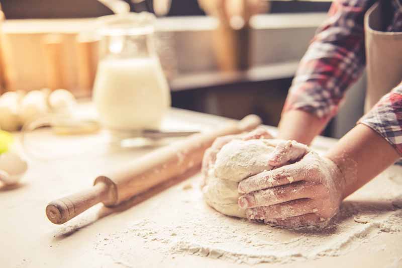 Horizontal image of a girl's hands kneading some bread dough on a table next to a rolling pin.