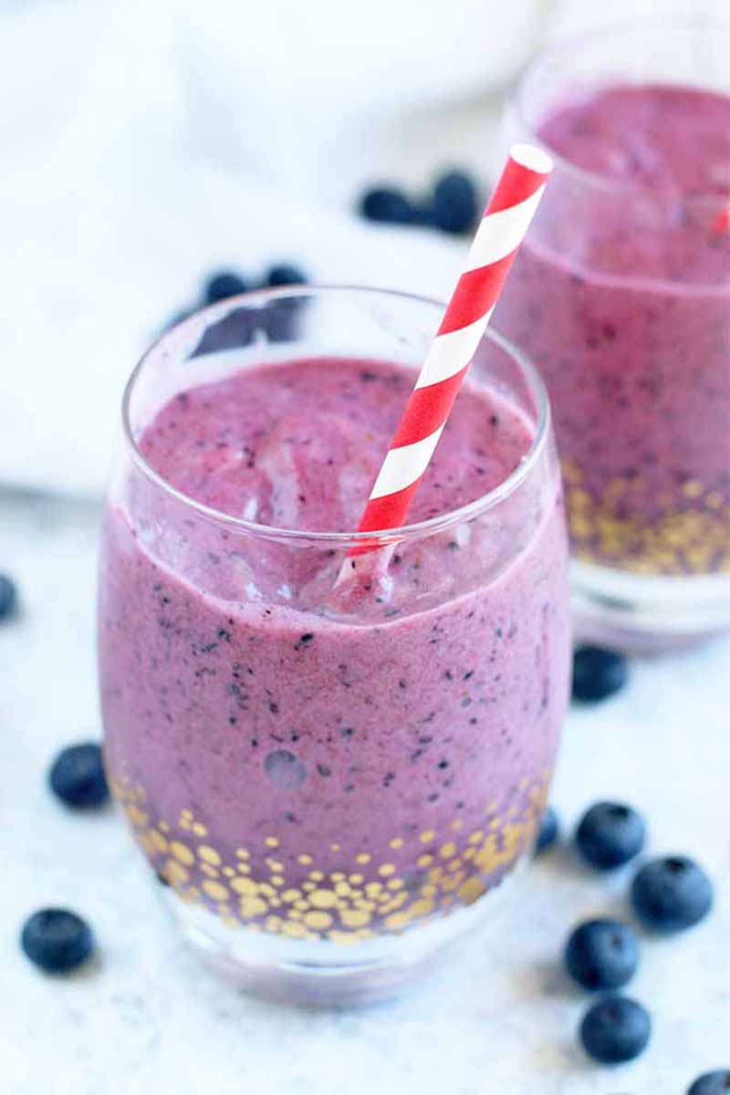 Vertical image of two glasses filled with a vibrant purple thick drink with a red straw.