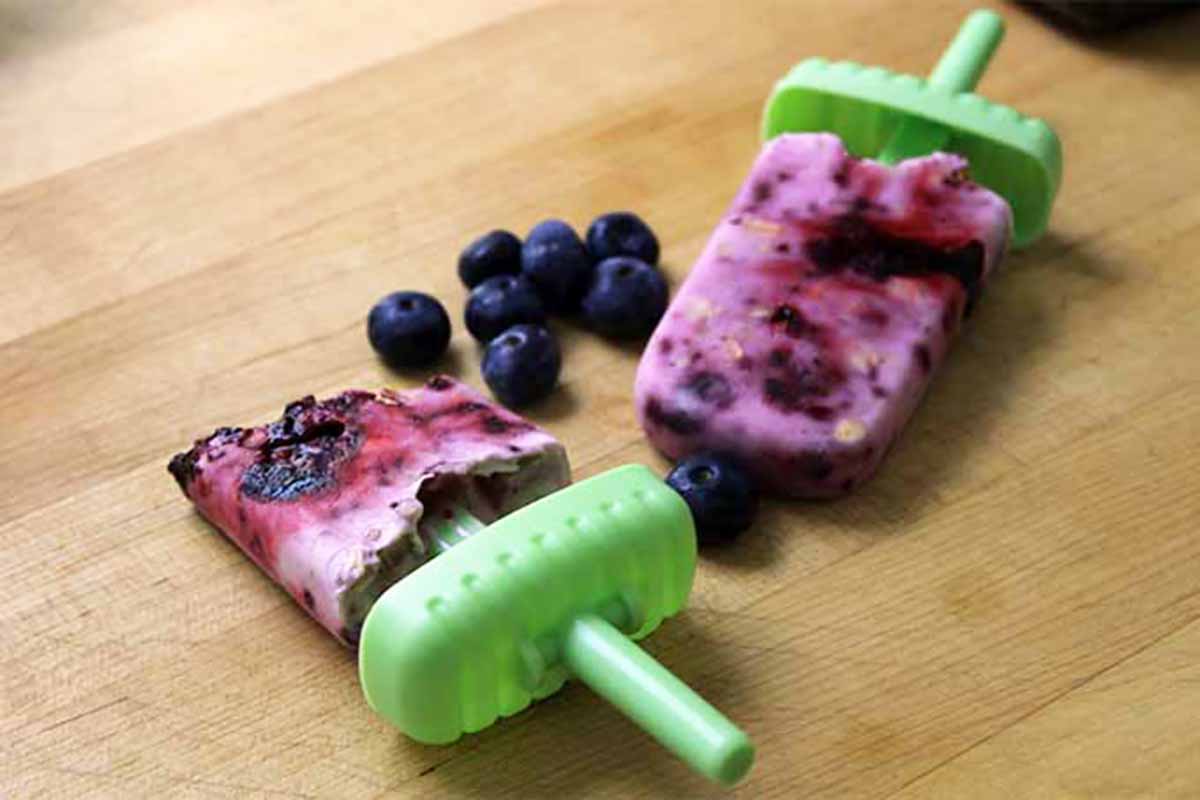 Horizontal image of two blueberry oat yogurt pops on a wooden table.