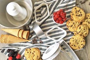 Horizontal image of assorted kitchen tools, cones, and cookies on a striped towel.