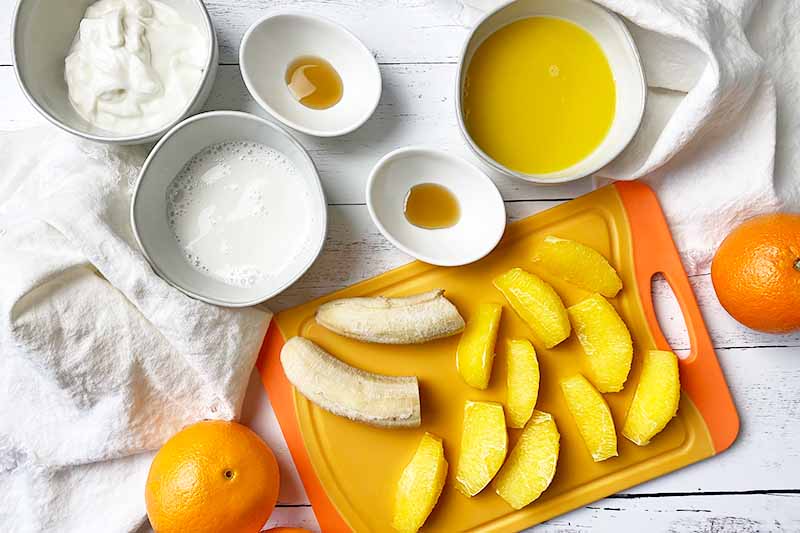 Horizontal image of prepped ingredients in bowls and sliced fresh fruit on a cutting board.