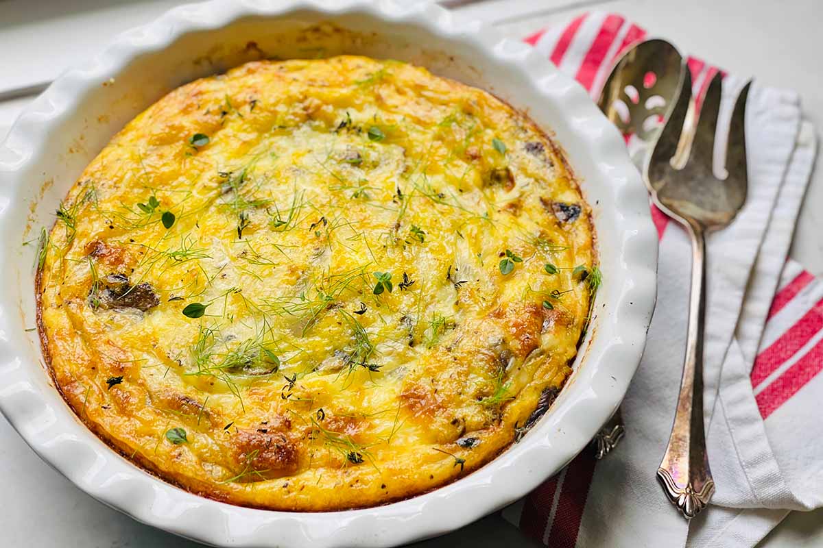 Horizontal image of a crustless quiche in a pie pan garnished with fresh dill.
