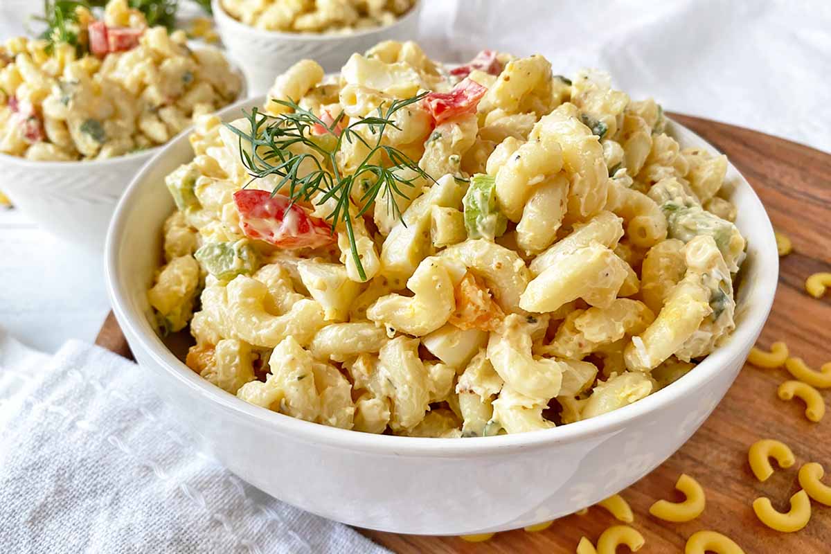 Horizontal image of a large bowl and two small bowls filled with a chilled macaroni dish garnished with dill fronds.