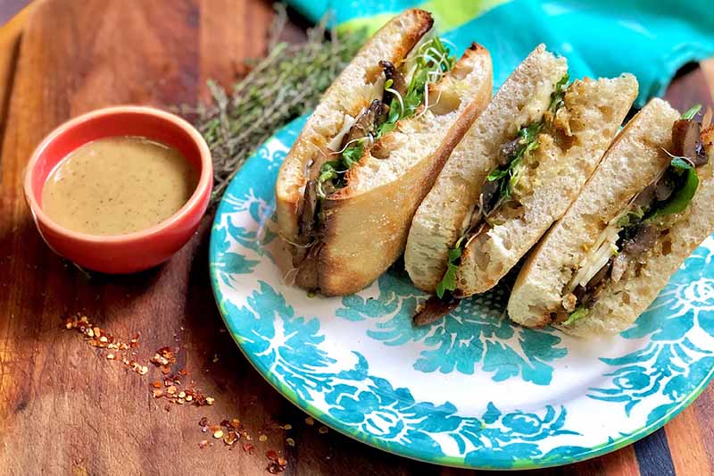 Horizontal image of vegetarian ingredients between bread slices on a blue plate next to a cup of spread.