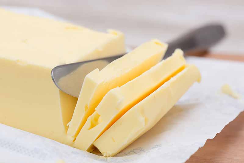 Horizontal image of a knife cutting into a block of butter on parchment paper.