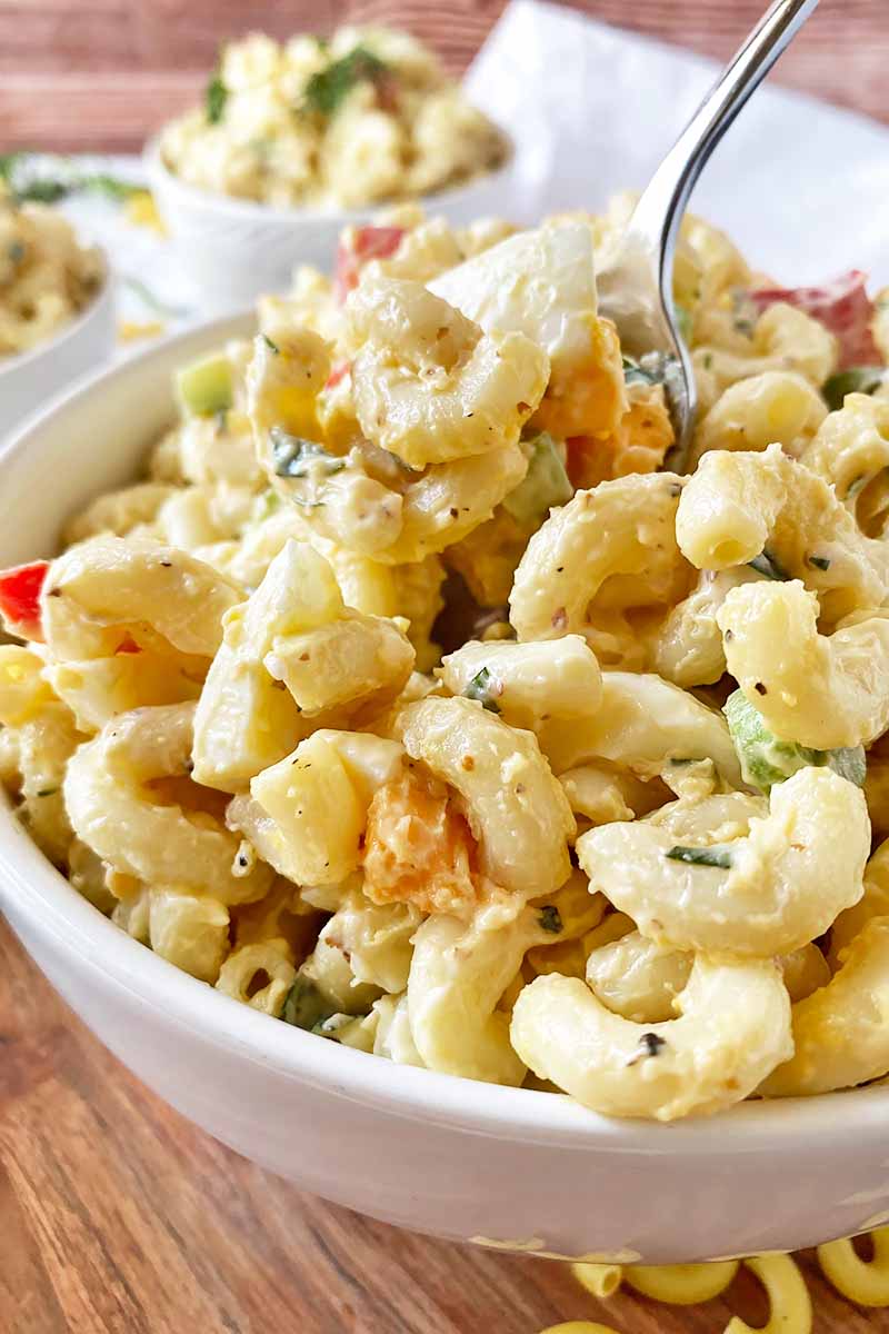 Vertical close-up image of a spoon inserted into a creamy pasta dish in a white bowl.