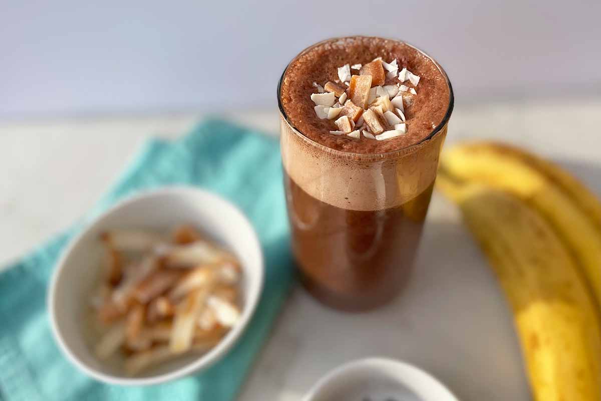 Horizontal image of a frothy coffee beverage in a glass cup garnished with toasted coconut chips.