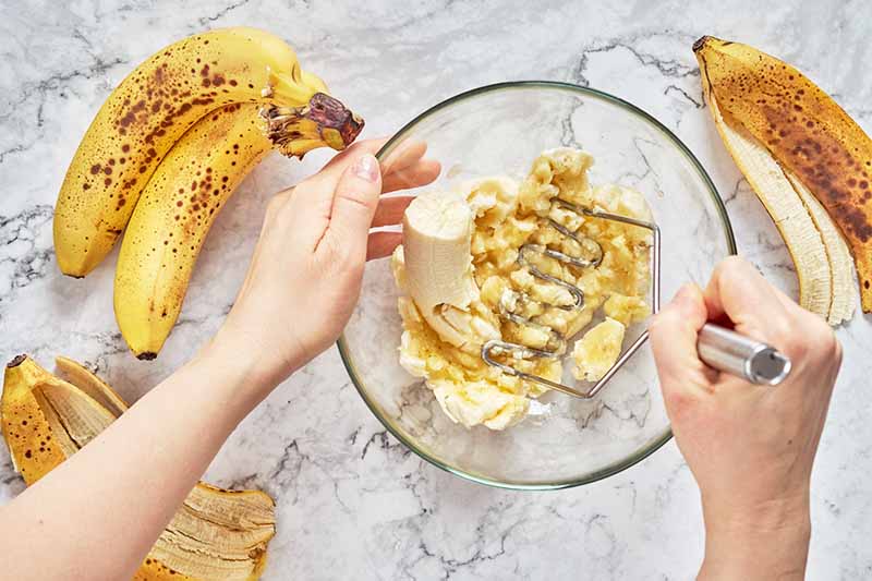 Horizontal image of mashing bananas in a glass bowl.