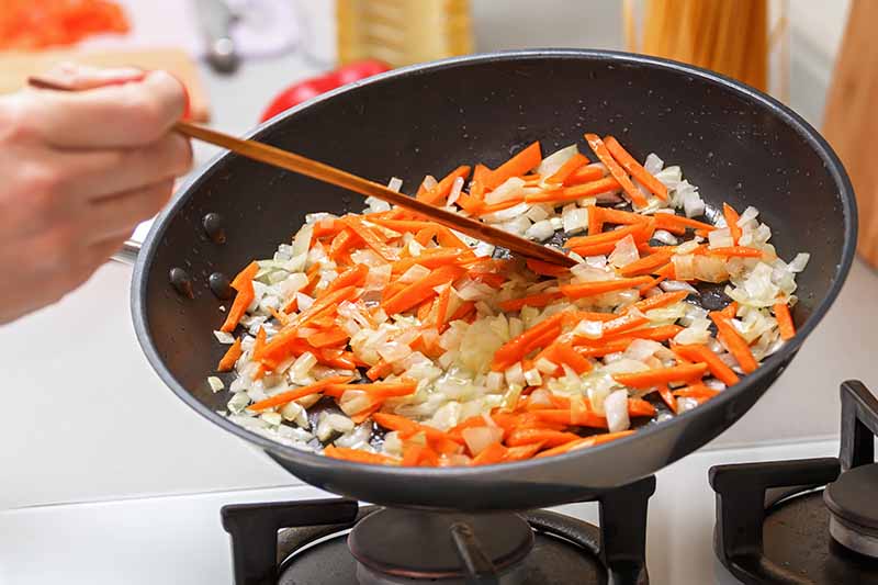 Horizontal image of cooking assorted colorful vegetables over the stovetop.