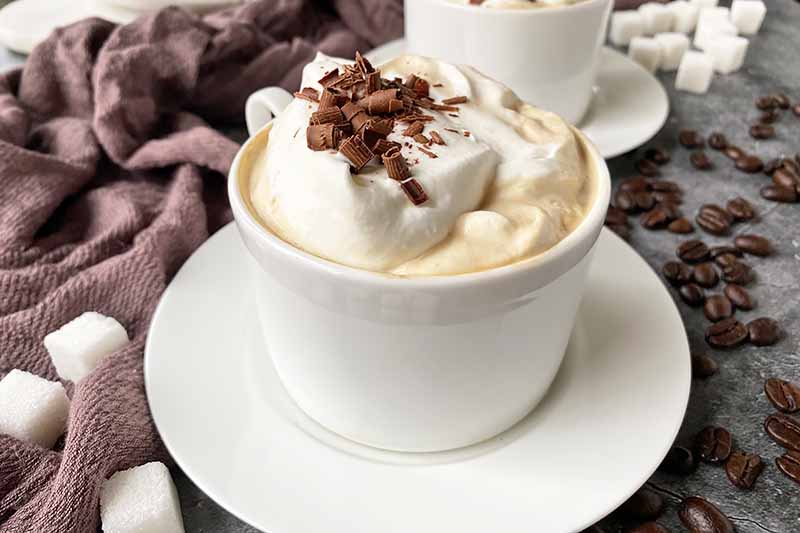 Horizontal image of two coffee beverages in white cups on plates.