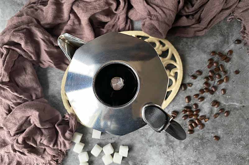 Horizontal image of a coffee maker next to sugar cubes and a tan towel.