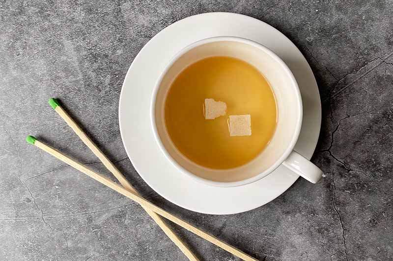 Horizontal image of a spirit and sugar cubes in a white mug next to matchsticks.