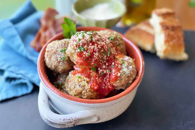Horizontal image of a dish filled with individual ground turkey mounds covered in marinara next to a blue towel and bread.