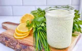 Horizontal image of a glass jar filled with an herb condiment next to lemons and parsley.