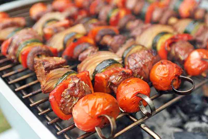Horizontal image of grilled balsamic lamb and vegetable sticks on the grill.