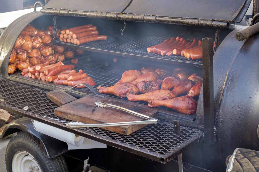 A side view of a large side wood burning smoker with cuts of meat on various racks.
