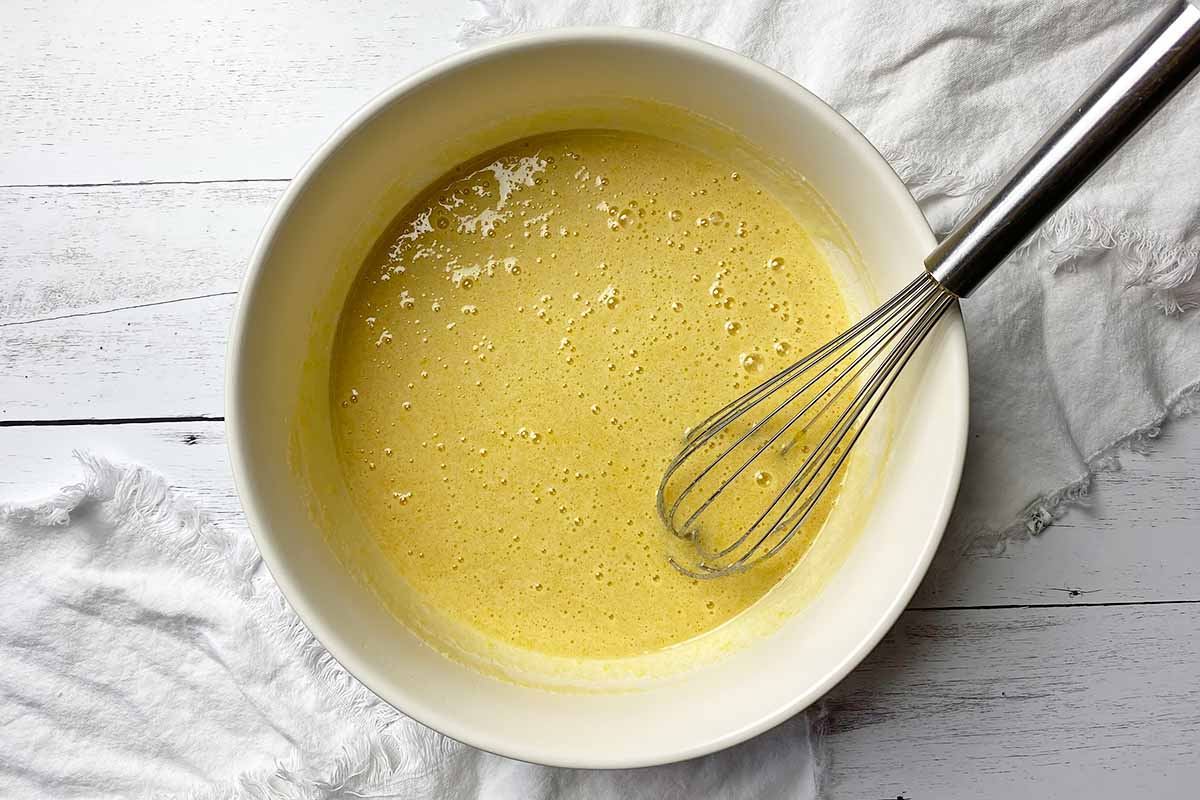 Horizontal image of whisking an egg and sugar mixture in a large white bowl.