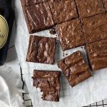 Horizontal image of portioned individual square baked goods on a parchment paper next to bottles of beer.