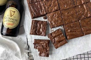 Horizontal image of portioned individual square baked goods on a parchment paper next to bottles of beer.