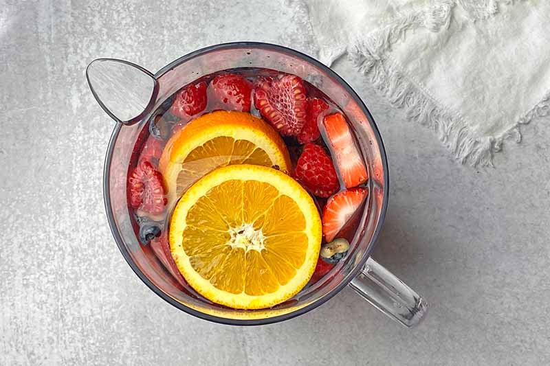 Horizontal image of a plastic clear pitcher filled with water and prepped produce.