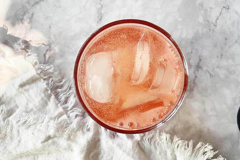 Horizontal image of ice cubes and a light pink liquid in a cup.