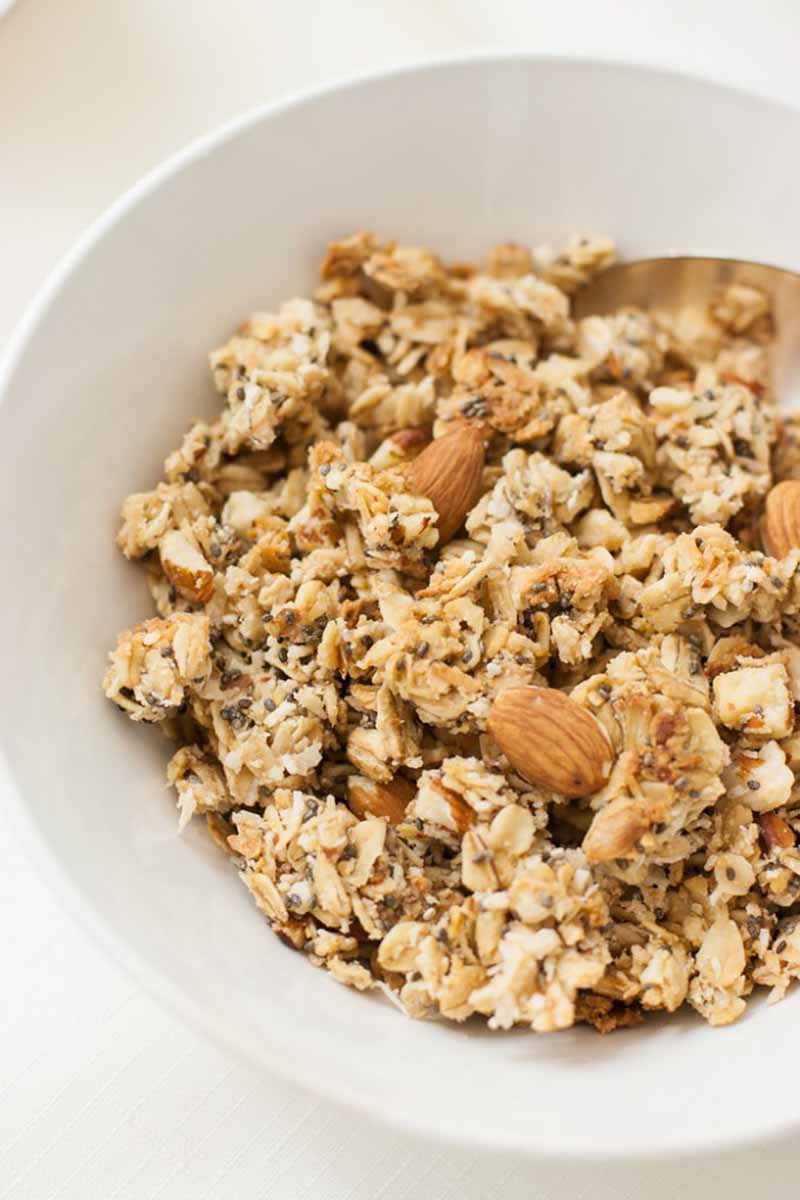 Vertical close-up image of a white bowl with nutty granola.