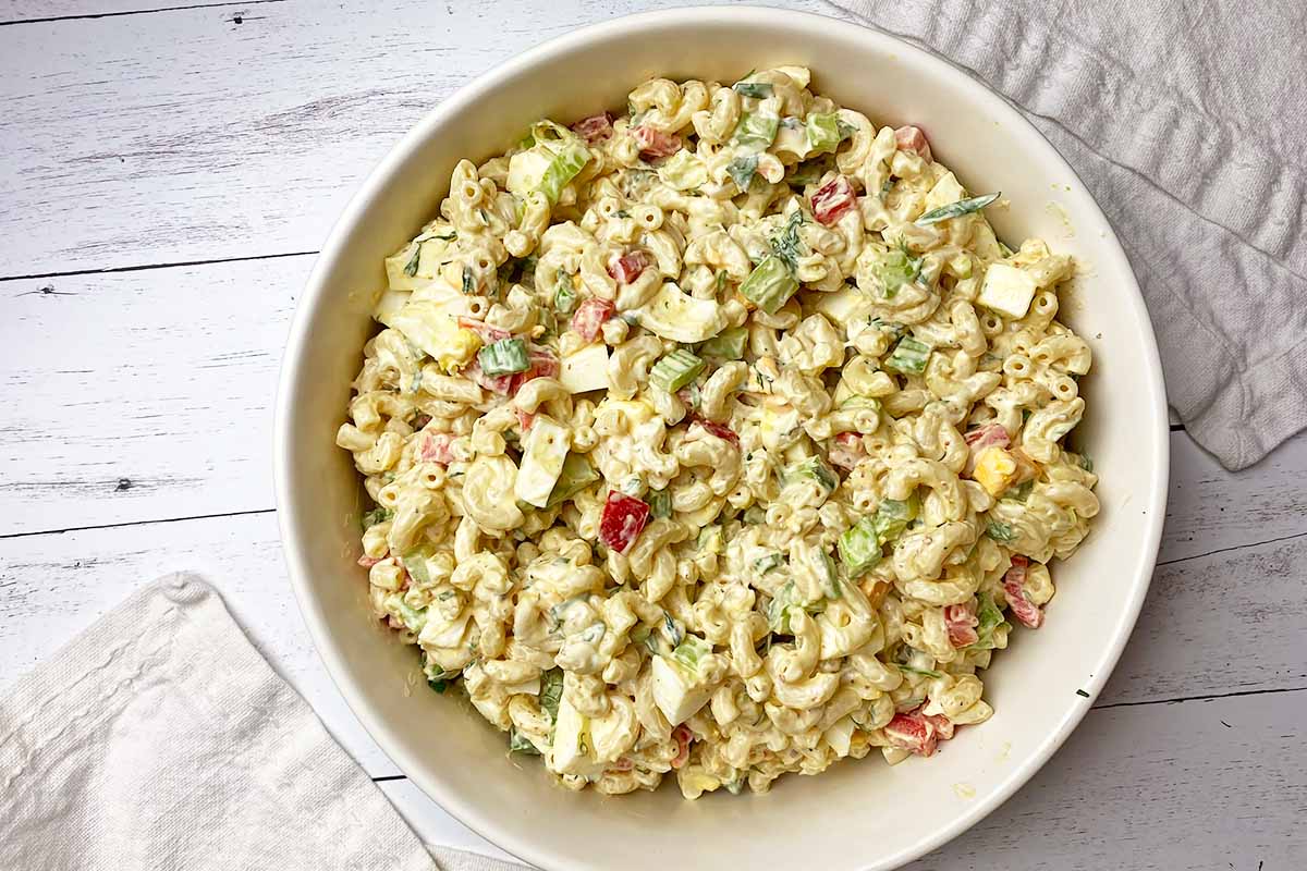 Horizontal image of a prepared macaroni salad in a large white bowl.