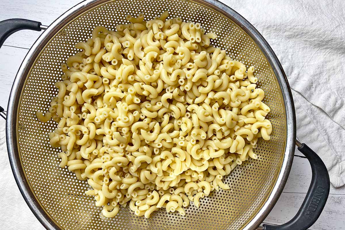 Horizontal image of cooked elbow pasta in a colander.