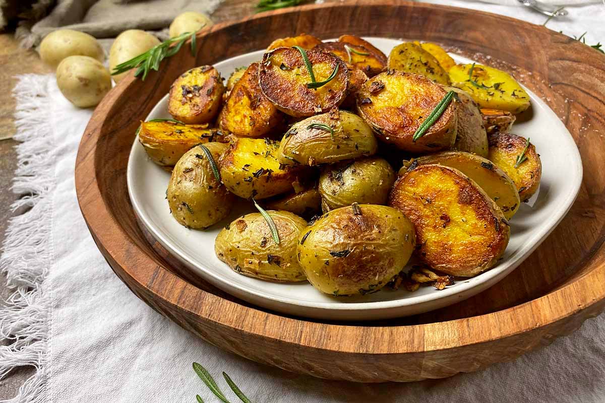 Horizontal image of a plateful of browned baby golds with fresh herbs on top of a wooden serving tray.