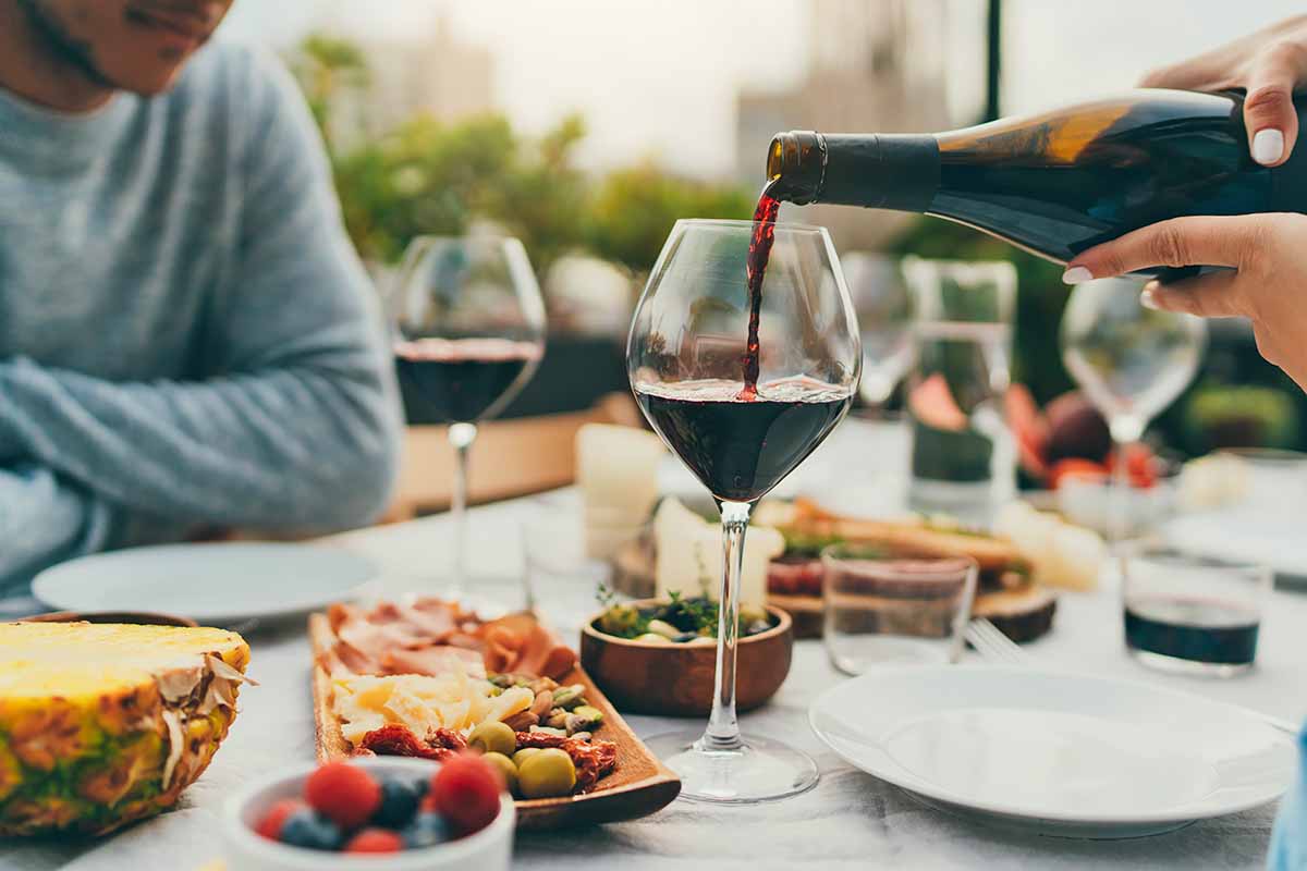Horizontal image of a dinner scene outside, with a woman pouring a drink for a man.
