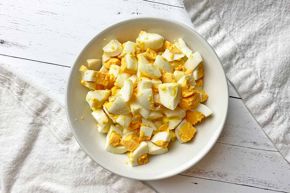 Horizontal image of chopped cooked eggs in a white dish.