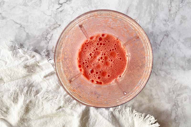 Horizontal image of a pink pureed liquid in a blender.