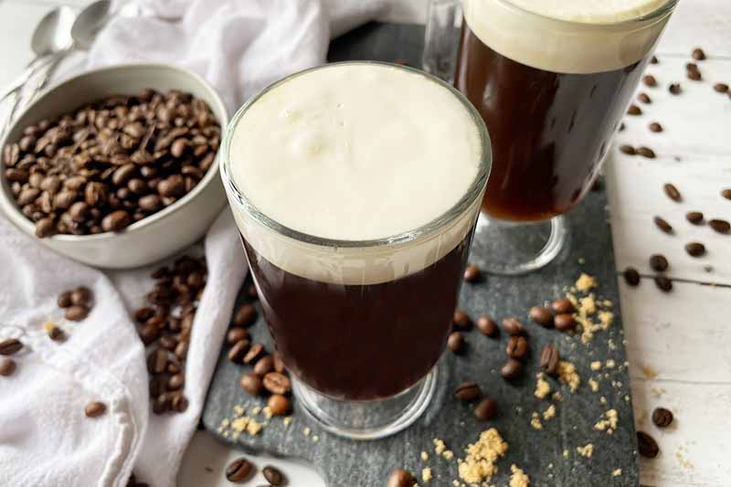 Horizontal image of two coffee beverages in glasses on a gray slate board.