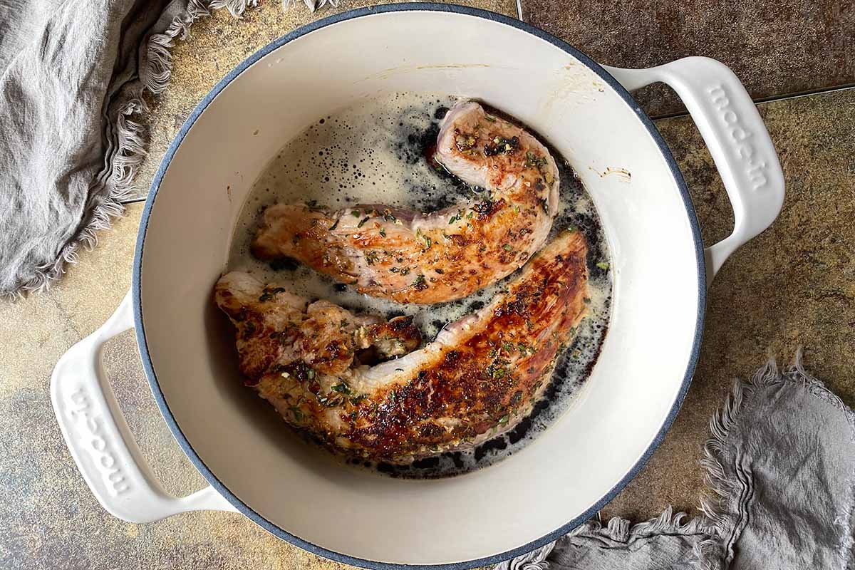 Horizontal image of cooking large pieces of meat in a dark stout in a Dutch oven.