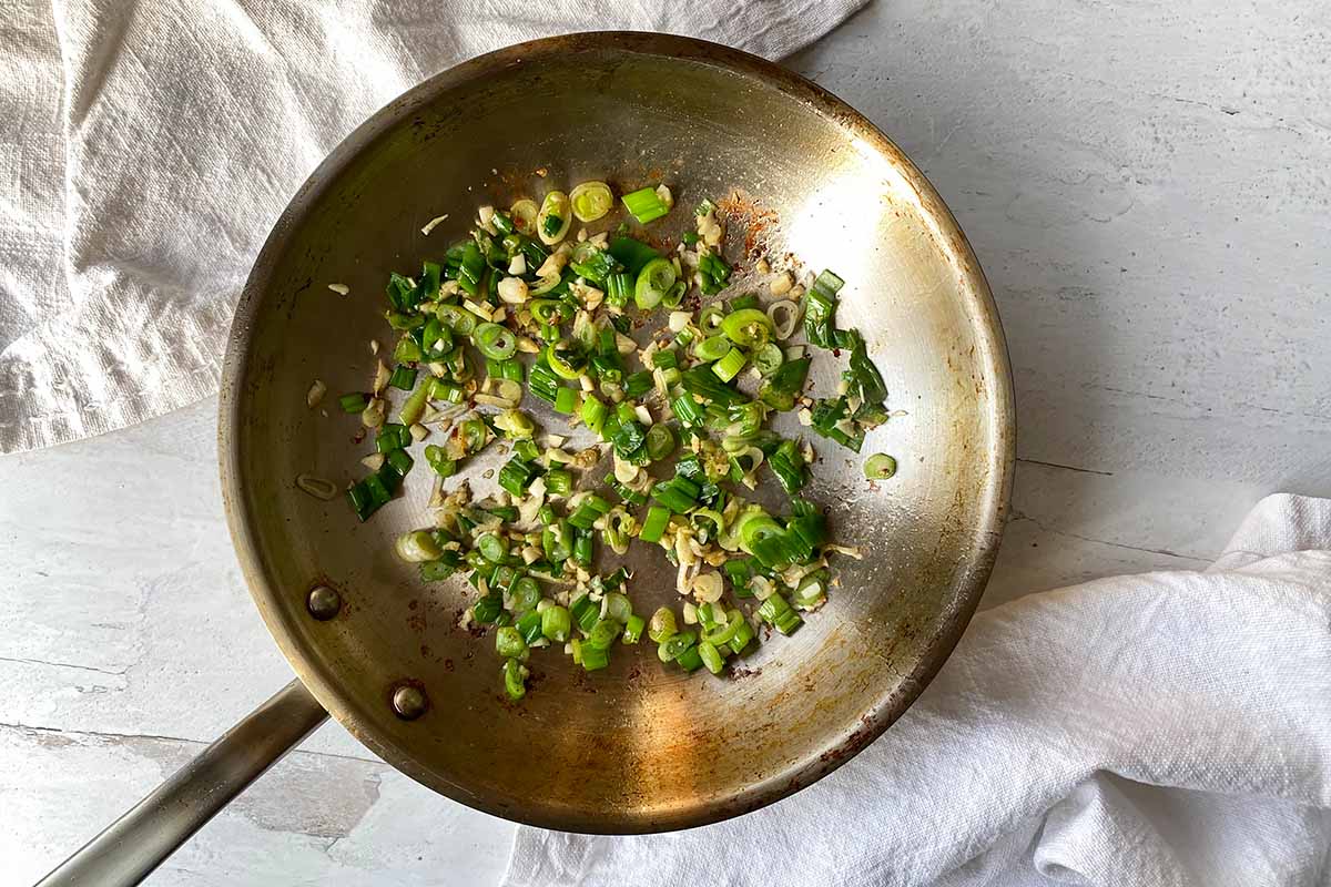 Horizontal image of cooking scallions and garlic in a pan.
