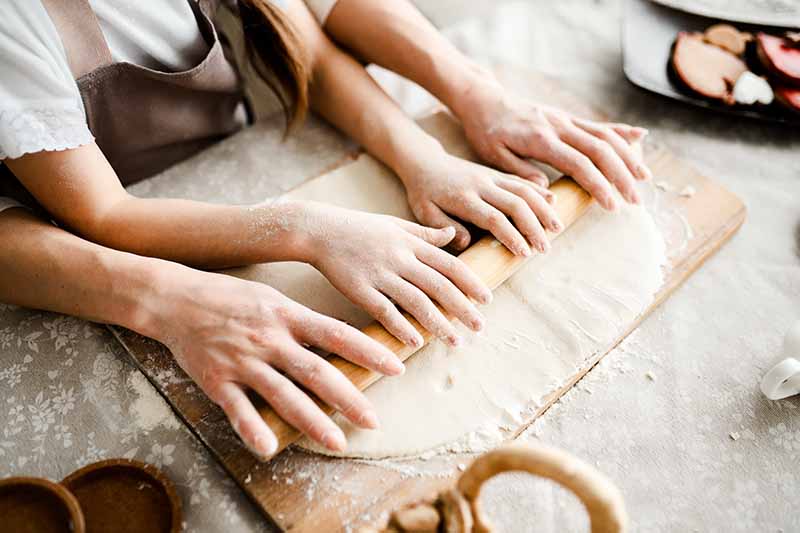 Horizontal image of a mother and daughter rolling out pastry dough on a floured countertop.