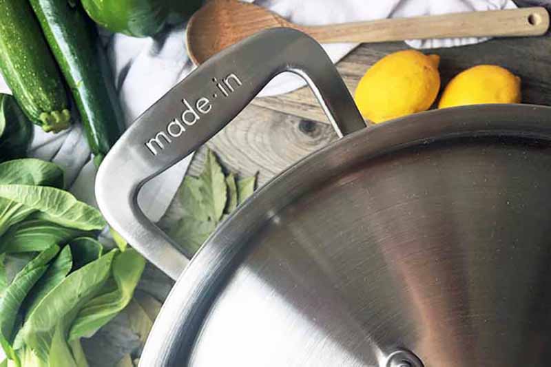 Horizontal close up image of a pot handle surrounded by vegetables and fruits.