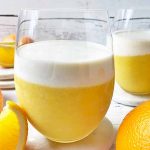 Horizontal image of glasses filled with a bright shake topped with a vanilla layer next to fresh fruit.