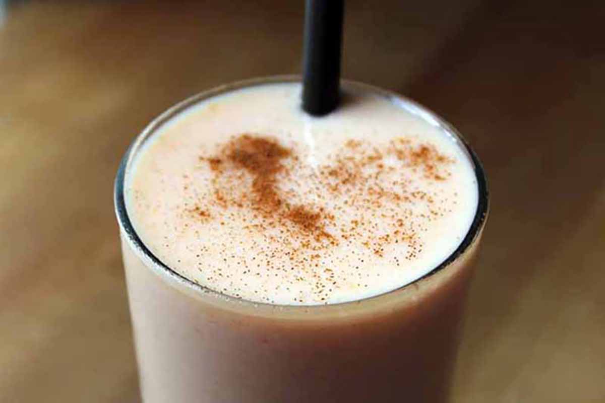 Horizontal close-up image of a glass filled to the brim with a papaya beverage, with a straw and cinnamon sprinkle.